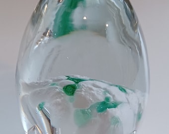 May include: A clear glass egg-shaped paperweight with a white and green swirl inside.