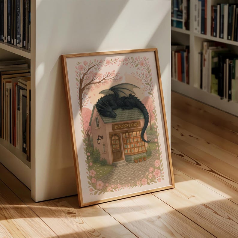 May include: Framed art print featuring a whimsical illustration of a black dragon resting on the roof of a quaint bookstore. The artwork is set in a soft, pastel-colored scene with cherry blossoms and a cobblestone path. The bookstore sign is visible.