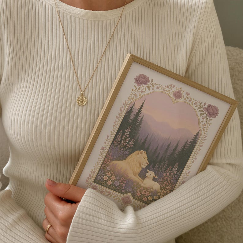 May include: A framed print featuring a lion and lamb in a floral meadow, with a forest backdrop. The print is held by a person wearing a white ribbed sweater and a gold pendant necklace.