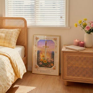May include: A framed print of a sword with a gold hilt and a blade, set against a backdrop of a sunset and flowers. The print is in a gold frame and is titled "Kingsflame of Terraasen". The print is displayed next to a bed with a yellow plaid pillow and a nightstand.