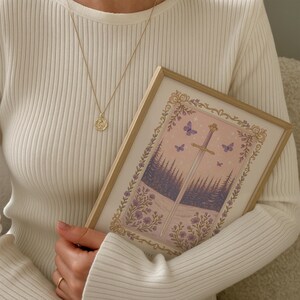 May include: A gold pendant necklace and a framed art print. The print features a sword, butterflies, and a forest scene in shades of purple, pink, and white. The frame is light-colored wood.