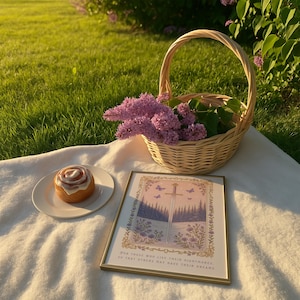 May include: A picnic scene with a woven basket filled with purple flowers, a framed print with a sword illustration, and a cinnamon roll on a white plate. The print has the text: "For those who live their nightmares, so that others may have their dreams."