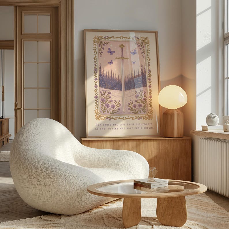 May include: A framed art print with a sword, butterflies, and forest scene. The print has a gold frame and the text: "FOR THOSE WHO LIVE THEIR NIGHTMARES SO THAT OTHERS MAY HAVE THEIR DREAMS." The room features a white chair, wooden table, and a lamp.