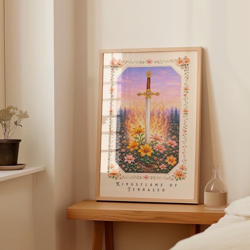May include: Framed art print featuring a sword with a gold hilt, set against a fiery background and floral foreground. The artwork is enclosed in a light wood frame and includes the text "Kingsflame of Terrasen".
