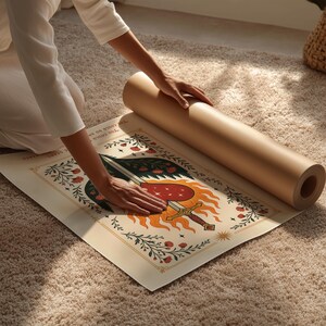 Op de afbeelding: Een opgerolde bruine papieren poster naast een gedeeltelijk uitgerolde poster op een beige tapijt. De poster heeft een centraal ontwerp van een hart, zwaard en vlammen, met bloem- en tekstelementen in rood, groen en goud.