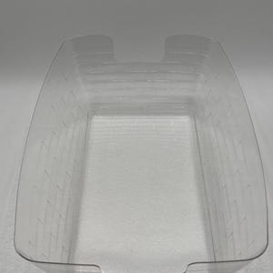 May include: A clear, rectangular plastic container with a series of horizontal ridges and two cut-out handles. The container is transparent, allowing visibility of its contents. The design suggests it is for storage or organization.