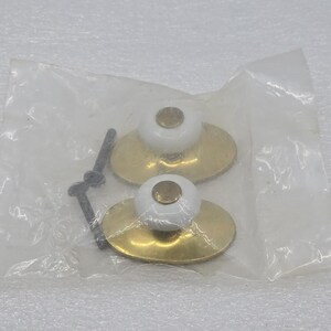 May include: Two white and gold cabinet knobs with a brass finish, packaged in a clear plastic bag. Each knob features a white, rounded top and a gold-colored base. A black screw is also included.