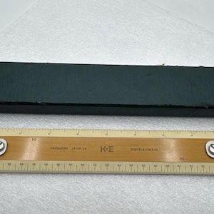 May include: A vintage wooden ruler with metal accents and a dark green box. The ruler is marked with measurements in inches and features a unique design. The box is rectangular and appears to be made of a textured material.