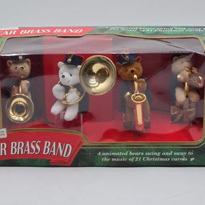 May include: A Bear Brass Band boxed set featuring four animated plush bears wearing blue uniforms and hats. Each bear holds a gold-colored musical instrument. The box displays the text Bear Brass Band and states that the bears swing and sway to the music of 21 Christmas carols.