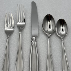 May include: A five-piece stainless steel flatware set consisting of a salad fork, dinner fork, dinner knife, soup spoon, and teaspoon. Each piece features a polished finish with a tapered handle design and a decorative floral motif at the base.