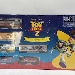 Puede incluir: Un set de tren eléctrico Disney Pixar Toy Story 2 Collector's Limited Edition Series One en una caja azul con Buzz Lightyear y Woody. El set incluye una locomotora roja y gris y cinco vagones de carga con gráficos de personajes.