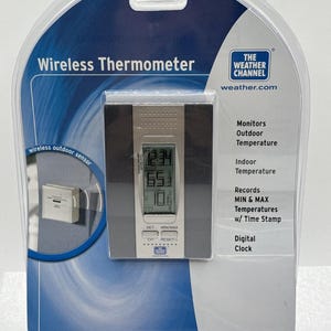 Puede incluir: Un termómetro inalámbrico digital plateado y negro de The Weather Channel en su empaque de plástico original. El dispositivo cuenta con una pantalla que muestra la hora y la temperatura, con botones etiquetados como SET, MIN/MAX, CH y RESET/+ al frente.