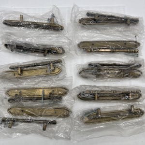May include: A collection of antique brass door handles, each individually wrapped in clear plastic. The handles have a detailed, ornate design and are likely for vintage or classic doors.