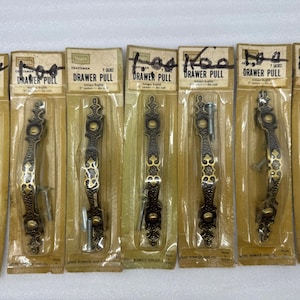 May include: A collection of Craftsman drawer pulls in their original packaging. The antique-style pulls are dark bronze with gold accents and measure 5 inches in length. Each pull is packaged with screws for installation.