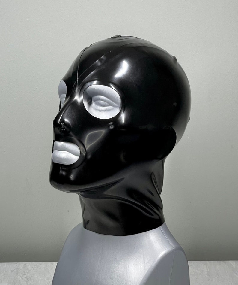 May include: A black latex mask with white eye and mouth openings. The mask is shiny and has a smooth texture.