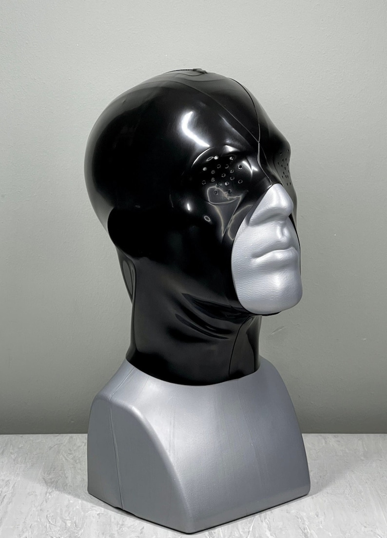 May include: A black latex hood with a single eye hole and a textured design. The hood is worn on a mannequin head.