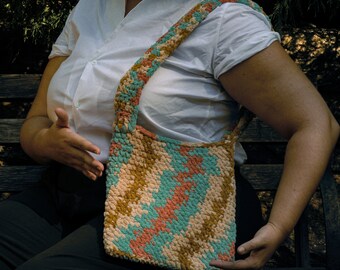May include: A crocheted shoulder bag with a colourful geometric pattern in shades of teal, peach, and beige.