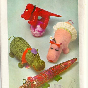 May include: Simplicity 6951 sewing pattern featuring stuffed animal designs. Includes a red dog balancing on a ball, a green hippo with a purple hat, a pink hippo with a lace collar, and a patterned alligator.