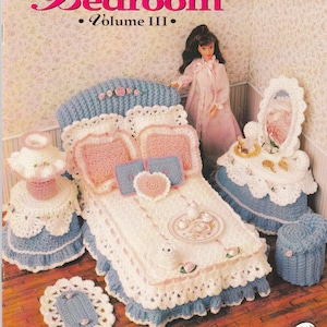 May include: A crocheted doll bedroom set in white, pink, and blue. The set includes a bed, vanity, lamp, and stool, all with intricate lace detailing. The bed has pink pillows and a heart-shaped accent. The image is from "Sweetheart Bedroom Volume III."