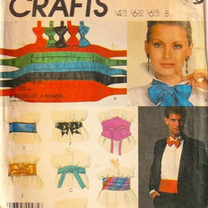 Peut inclure: Une pochette de patron de couture McCall's Crafts 2449 illustrant divers modèles de ceintures, cummerbunds et nœuds papillon. La couverture présente plusieurs styles, dont une ceinture bleue, un corset rose et une ceinture de smoking rouge.