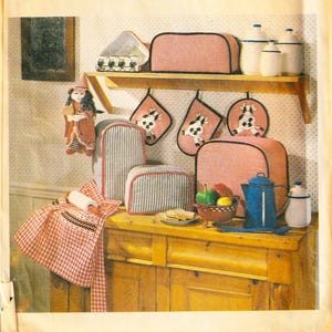 Peut inclure: Une collection d'accessoires textiles de cuisine comprenant des housses de grille-pain à rayures roses et bleues, des maniques roses avec des illustrations de vaches, un tablier à carreaux rouges et blancs et une housse de boîte à pain rose.