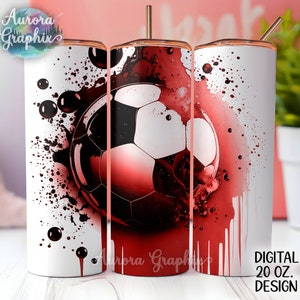 May include: A white 20 oz. tumbler with a soccer ball design. The design features a red and black soccer ball with a watercolor effect. The tumbler has a gold-colored lid and straw. The text "Aurora Graphix" is visible.