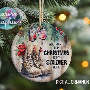 May include: A round Christmas ornament with a watercolor design of a pair of brown military boots, pine branches, red berries, and two dog tags. The text "All I want for Christmas is my soldier home" is written on the ornament.