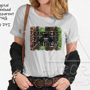 May include: A white t-shirt featuring a black panther graphic and the text "PANTHERS" repeated three times. The graphic is set against a green and brown background with a football field pattern.