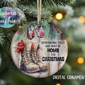 May include: A round, wooden Christmas ornament with a watercolor design. It features a pair of brown military boots, a red poinsettia, and two dog tags with the American flag. The text reads "Remembering those who won't be home for Christmas".
