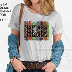 Könnte beinhalten: Weißes T-Shirt mit einem grafischen Design eines indianischen Kopfschmucks und dem Wort "INDIANS", das dreimal wiederholt wird. Die Grafik ist von einem grünen und blauen Fußballfeld-Design mit Yard-Linien umgeben.
