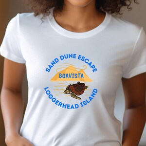 May include: White t-shirt with a blue and yellow graphic design that says "Sand Dune Escape Boa Vista Loggerhead Island" and features a sea turtle.