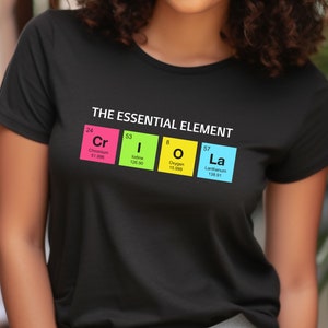 May include: Black t-shirt with the text "THE ESSENTIAL ELEMENT" and the periodic table elements Cr, I, O, and La in colorful boxes. The shirt features the atomic numbers, element symbols, and atomic weights.