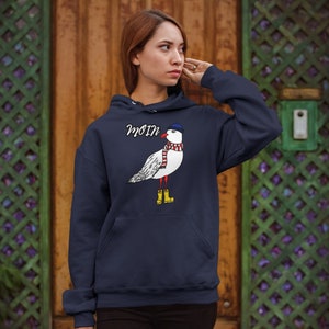 May include: A navy blue hoodie with a white seagull wearing a blue hat and red scarf. The seagull is wearing yellow rain boots. The hoodie has a pocket on the front and the word "Moin" printed on the front.