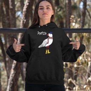 May include: Black hooded sweatshirt with a white seagull wearing a blue and red striped scarf and a blue hat. The seagull is wearing yellow rain boots. The text "Moin" is printed on the sweatshirt.