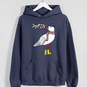 May include: A navy blue hoodie with a white seagull wearing a blue hat and red and white scarf. The seagull is wearing yellow rain boots. The hoodie has the word "Moin" printed on it.