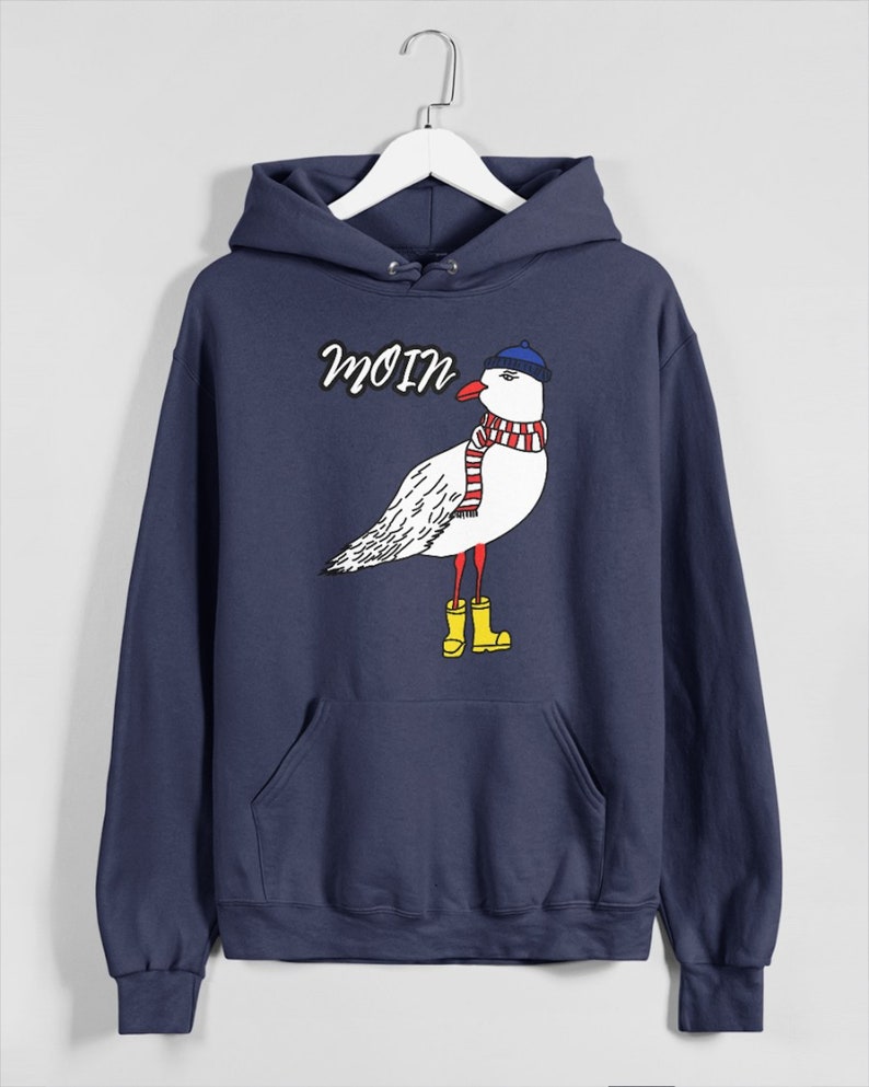 May include: A navy blue hoodie with a white seagull wearing a blue hat and red and white scarf. The seagull is wearing yellow rain boots. The hoodie has the word "Moin" printed on it.
