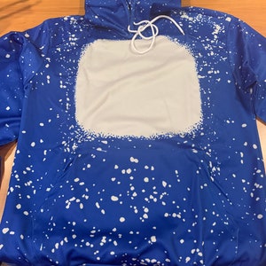 May include: A blue hoodie with a white splatter pattern and a large white square on the front. The hoodie has a drawstring hood.