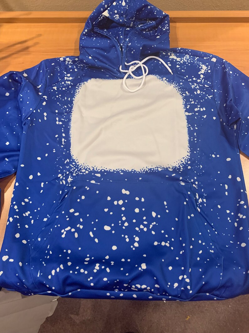 May include: A blue hoodie with a white splatter pattern and a large white square on the front. The hoodie has a drawstring hood.