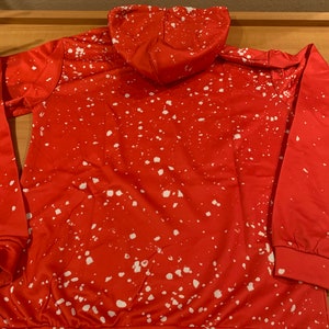 K&ouml;nnte beinhalten: Roter Kapuzenpullover mit einem wei&szlig;en Spr&uuml;hfarben-Design.