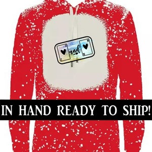 K&ouml;nnte beinhalten: Roter Hoodie mit einem wei&szlig;en Spritzmuster. Der Hoodie hat eine wei&szlig;e K&auml;ngurutasche mit einer Grafik von zwei Spielkarten, einer 2 Herz und einer 10 Herz, mit dem Wort "and" dazwischen.