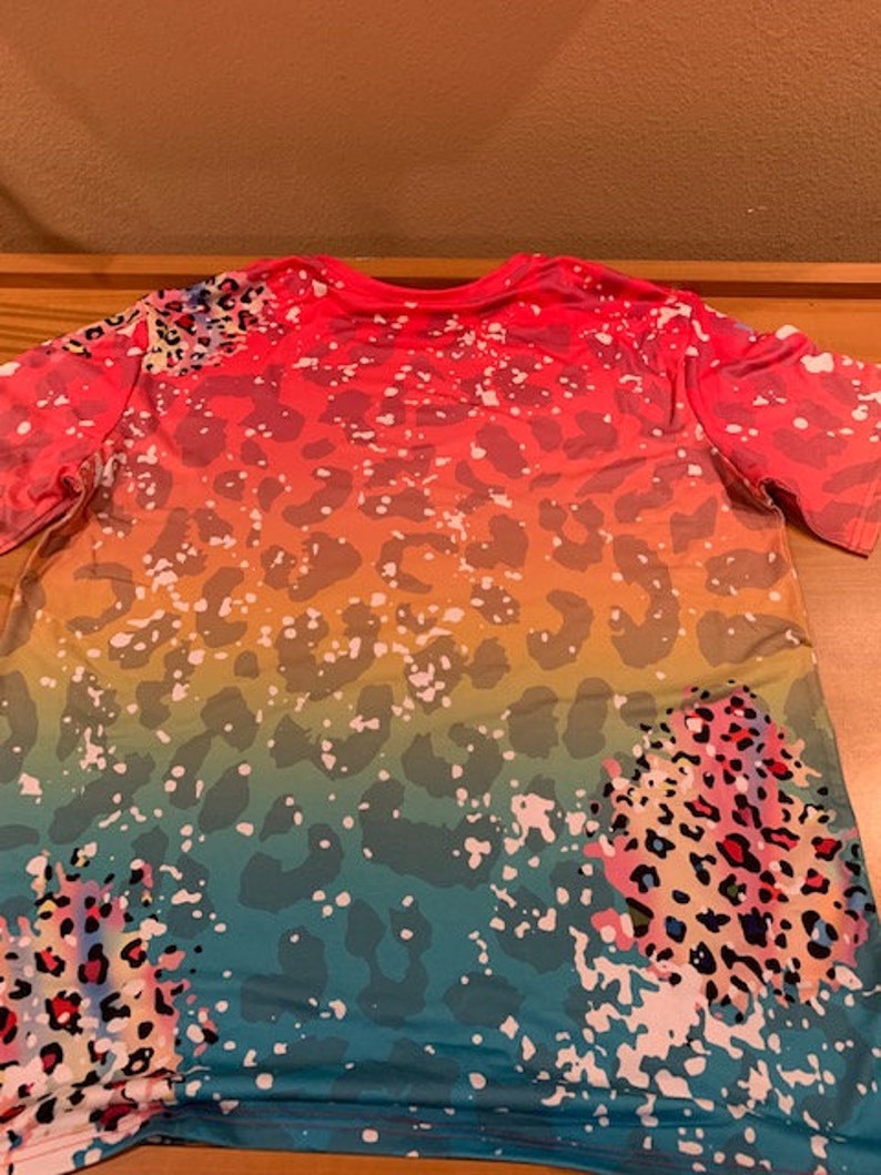 May include: A colorful t-shirt with a rainbow ombre design and leopard print. The shirt has a relaxed fit and short sleeves.