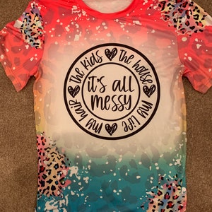 May include: A pink, blue, and white t-shirt with a leopard print design. The shirt has a white circle with the text "The kids are the house it's all messy my life my way" in black.