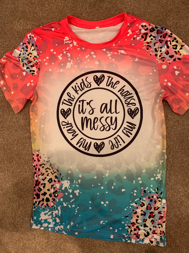 May include: A pink, blue, and white t-shirt with a leopard print design. The shirt has a white circle with the text "The kids are the house it's all messy my life my way" in black.