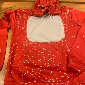 K&ouml;nnte beinhalten: Roter Hoodie mit einem wei&szlig;en Spr&uuml;hfarben-Design. Der Hoodie hat ein gro&szlig;es wei&szlig;es Quadrat auf der Vorderseite mit einem Kordelzug.
