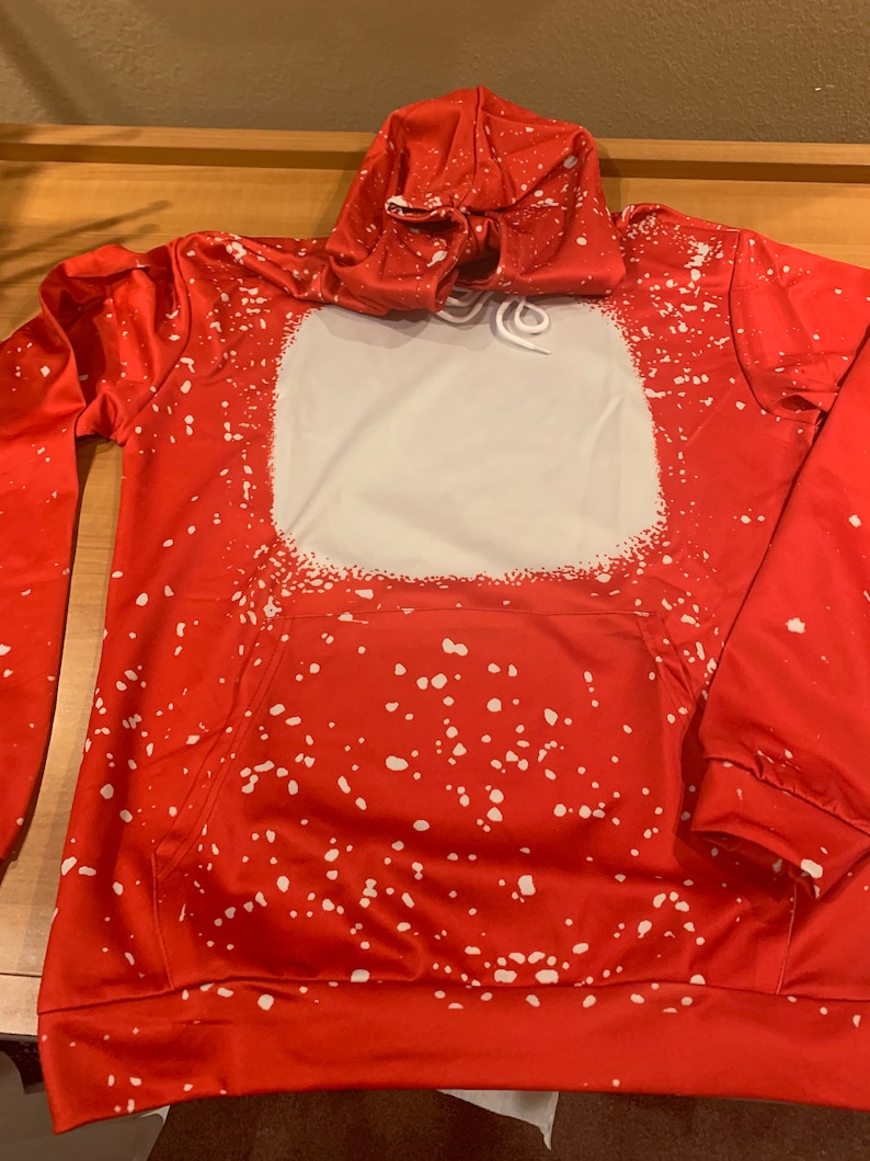 K&ouml;nnte beinhalten: Roter Hoodie mit einem wei&szlig;en Spr&uuml;hfarben-Design. Der Hoodie hat ein gro&szlig;es wei&szlig;es Quadrat auf der Vorderseite mit einem Kordelzug.