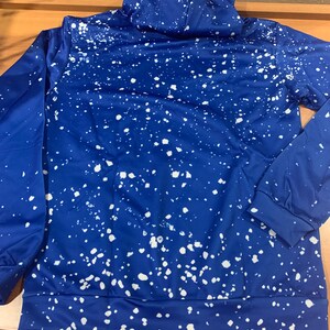 May include: A blue hoodie with a white splatter paint design. The hoodie has a drawstring hood and long sleeves.