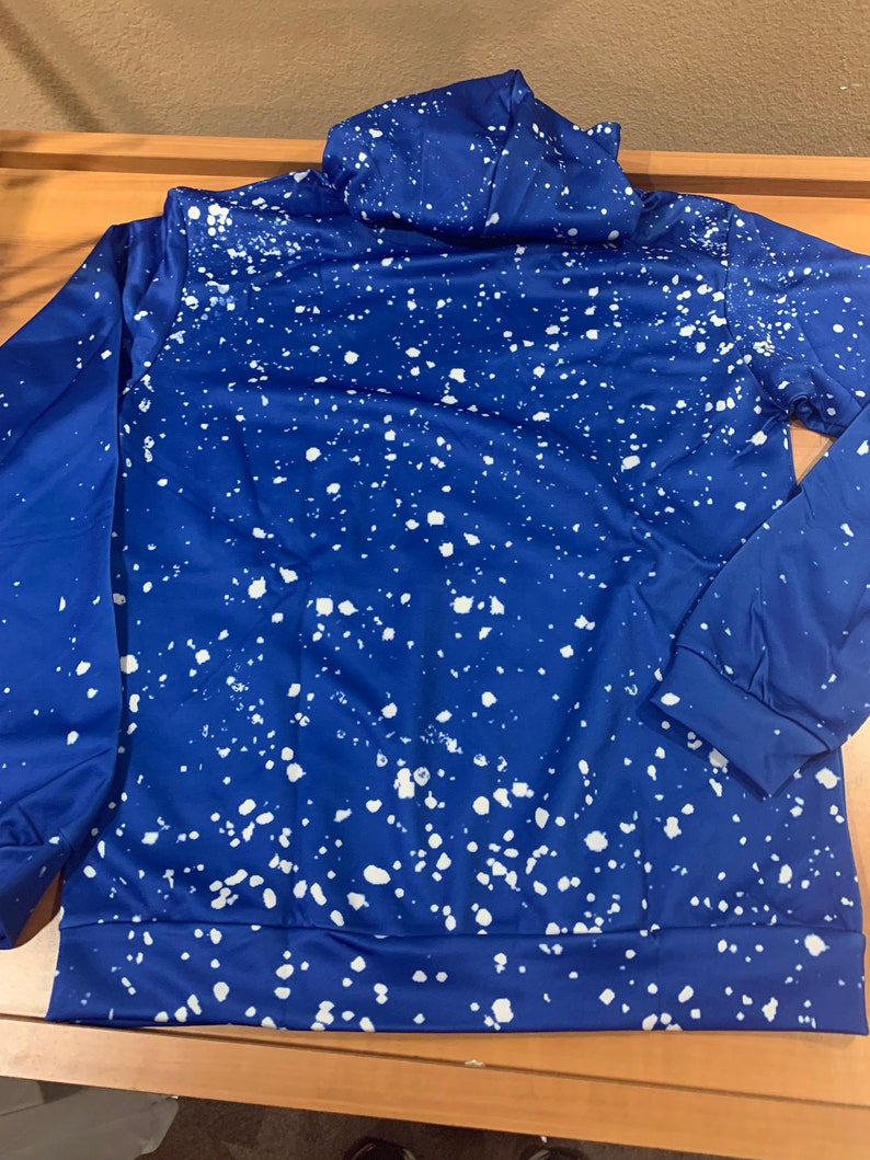 May include: A blue hoodie with a white splatter paint design. The hoodie has a drawstring hood and long sleeves.