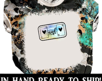 May include: A white t-shirt with a tie-dye pattern in shades of black, brown, and teal. The shirt features a graphic of two playing cards, a 2 of hearts and a 10 of hearts, with the word "and" between them.