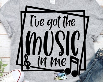 Può includere: Una maglietta grigia con testo nero che recita "Ho la musica dentro di me" all'interno di una cornice quadrata nera. Un pentagramma e una nota musicale sono inclusi anche nel design.