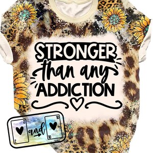 Puede incluir: Una camiseta de color crema con estampado de leopardo y diseño de girasol. La camiseta tiene el texto "STRONGER than any ADDICTION" con un símbolo de corazón.